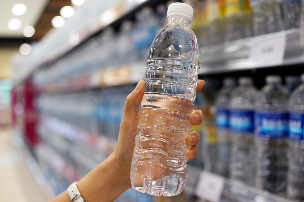 Iemand pakt een fles drinkwater uit het schap in de supermarkt