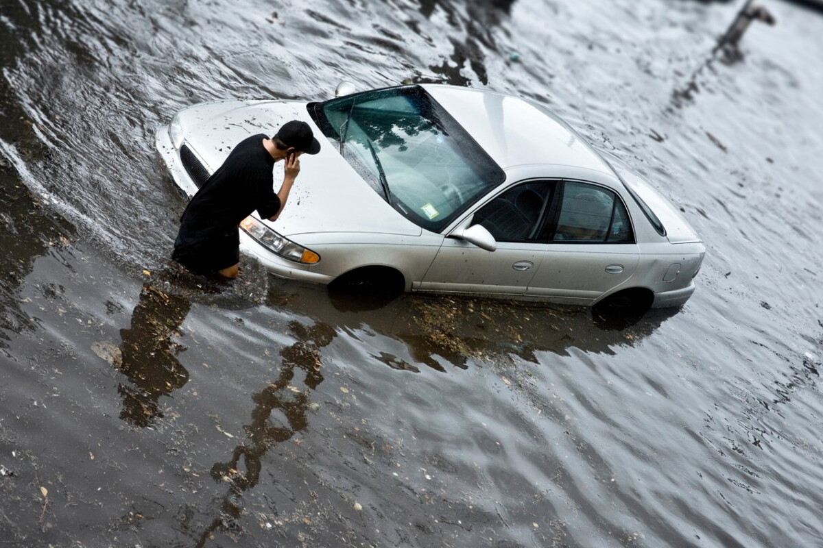 Man bij auto in onder water gelopen straat