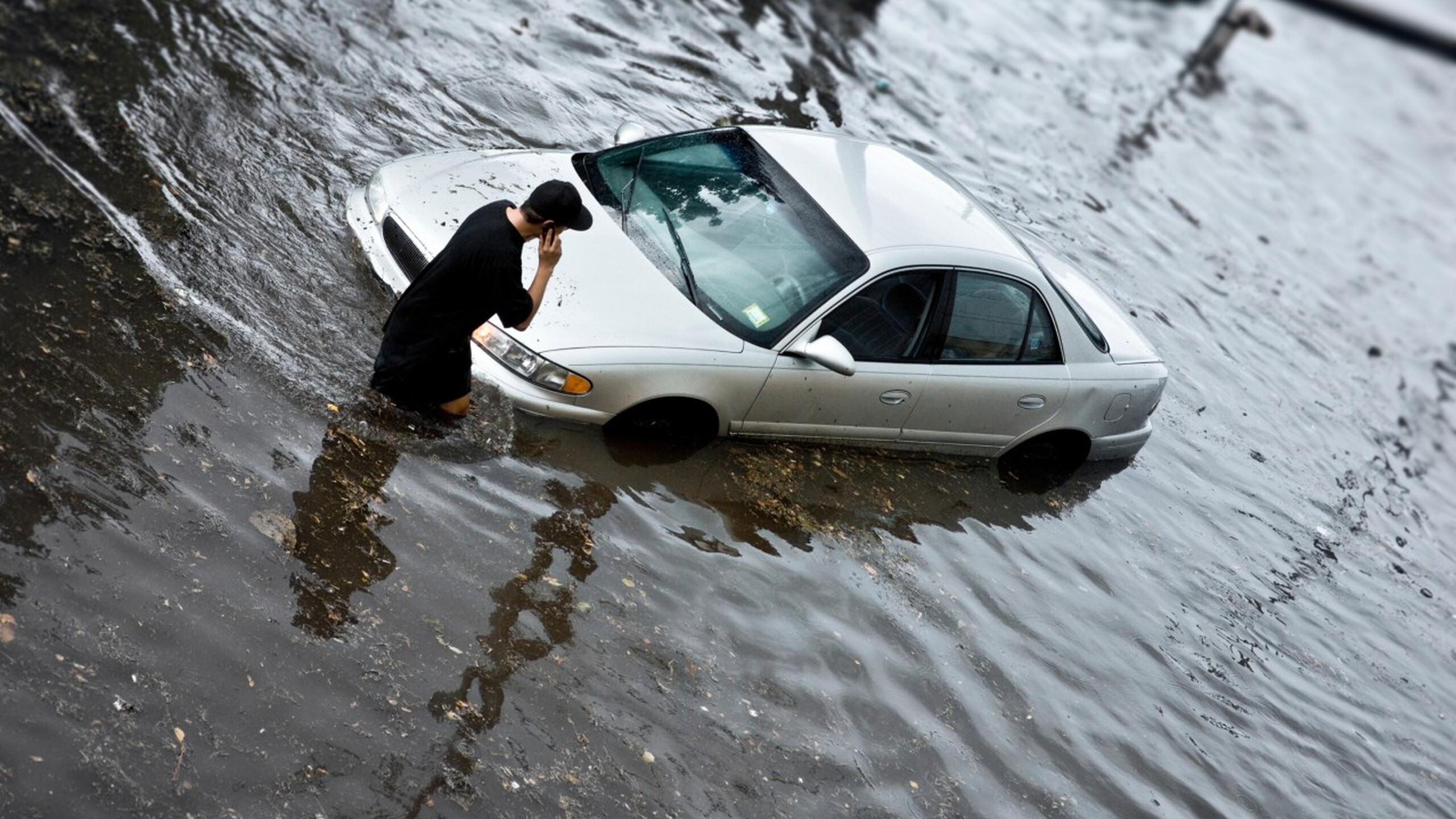 Man bij auto in onder water gelopen straat